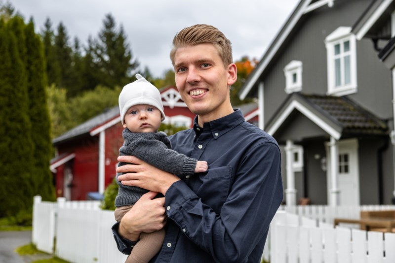 Ung familiefar med baby utenfor grått hus