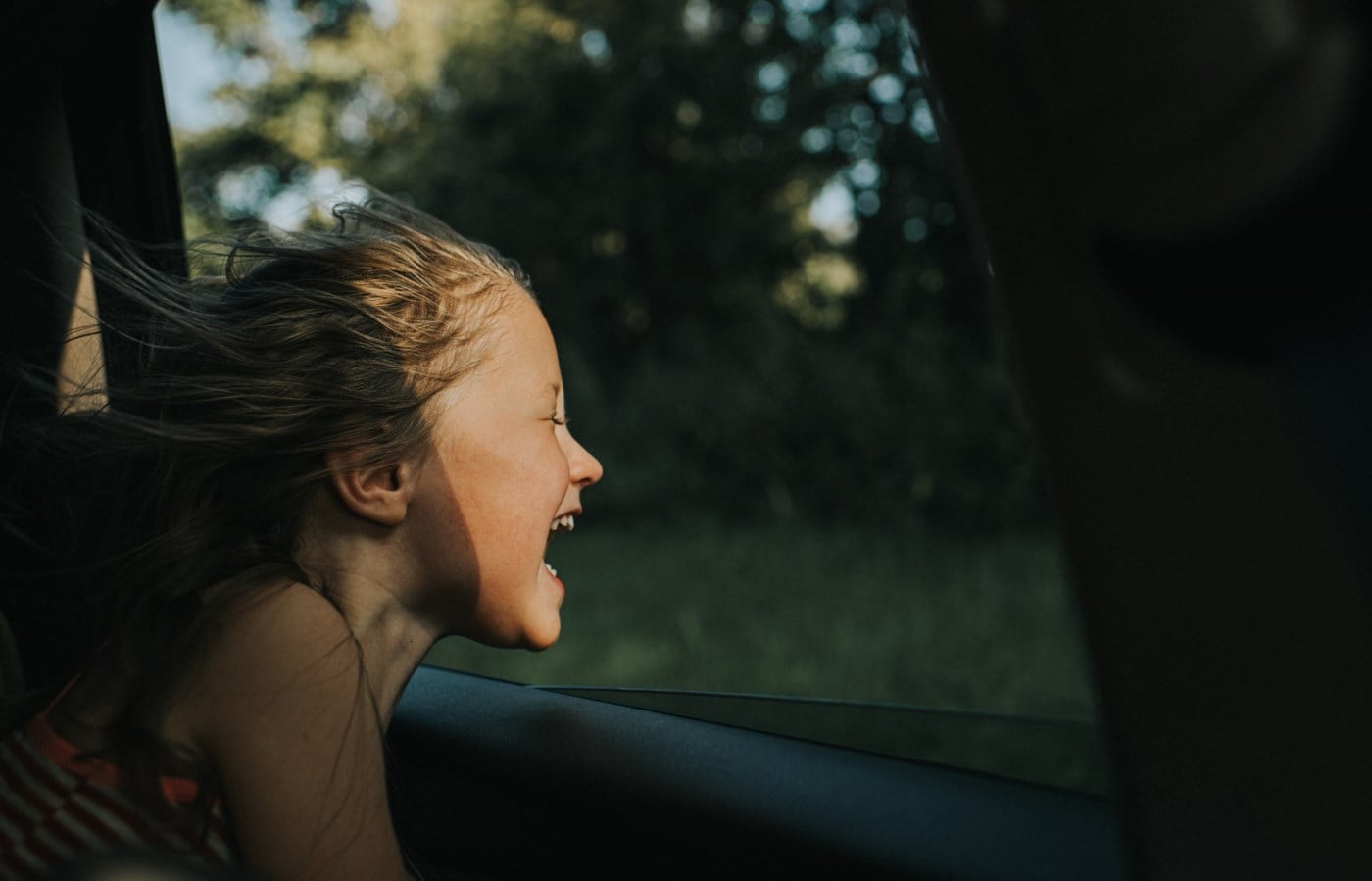 Liten jente smiler mens hun peker ansiktet ut av et bilvindu